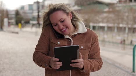 Smiling-mature-woman-holding-tablet-and-talking-on-phone